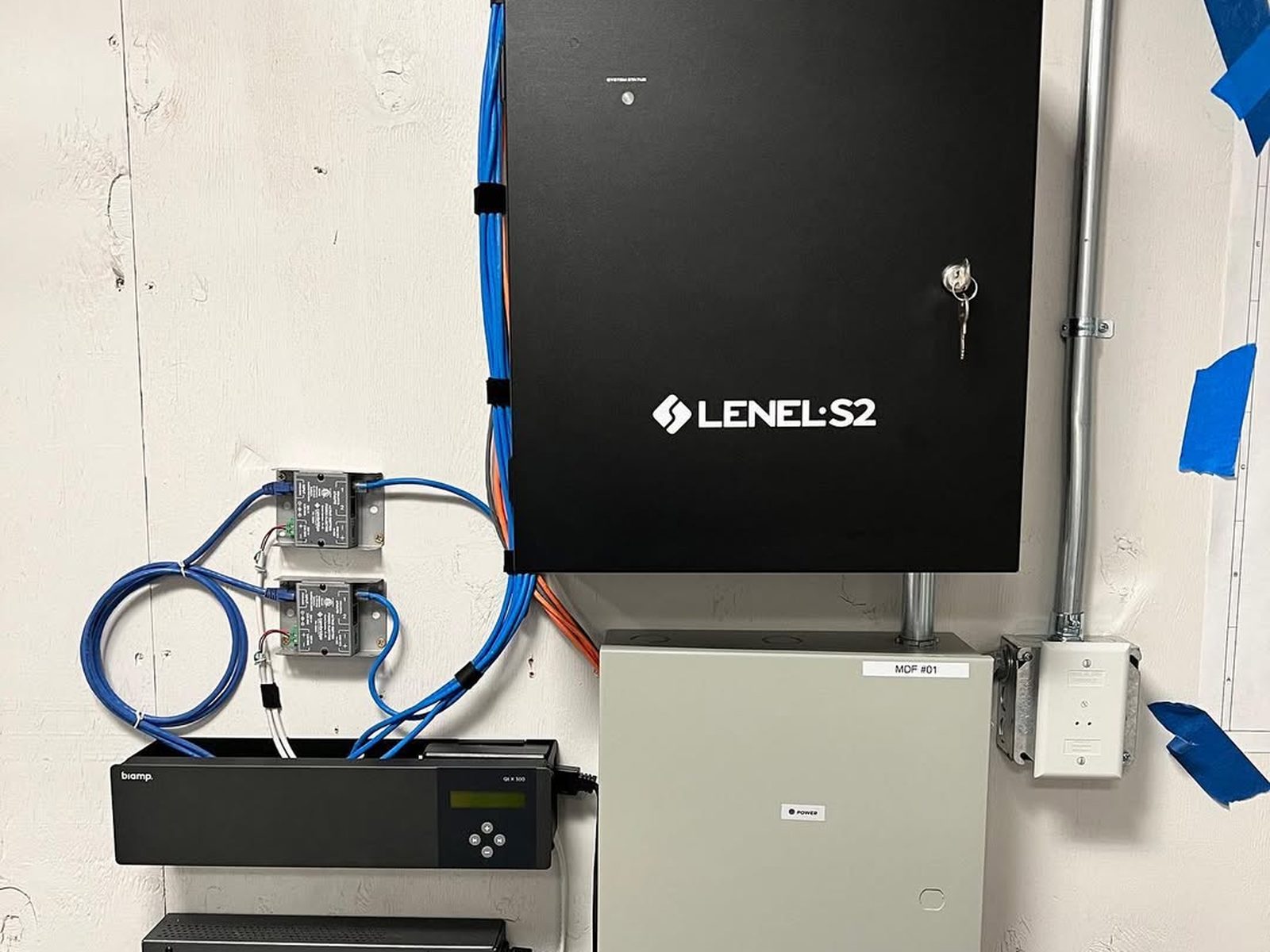Lenel S2 access control panel mounted on a wall beside its power supply and battery backup
