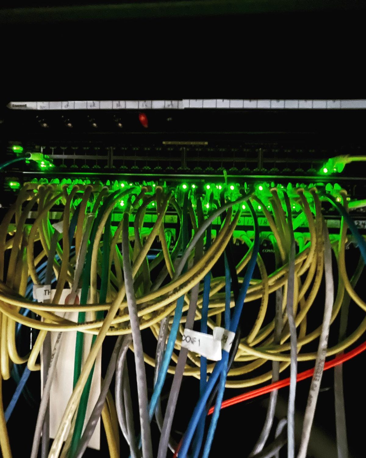 Network cabinet before cleanup, with tangled unlabeled patch cords hanging loose across the switch