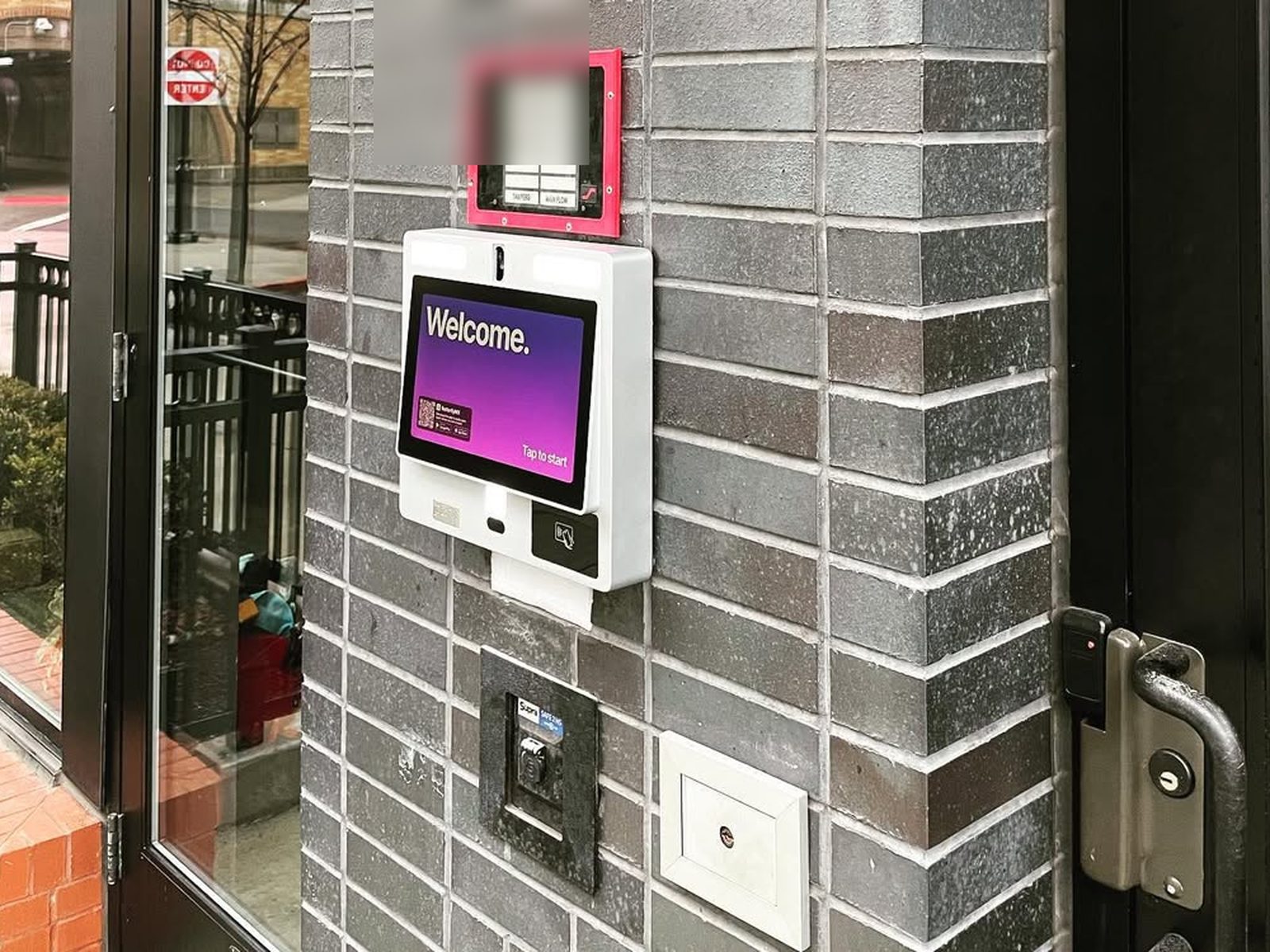 ButterflyMX video intercom panel mounted on a brick entry pillar next to a glass door and card reader