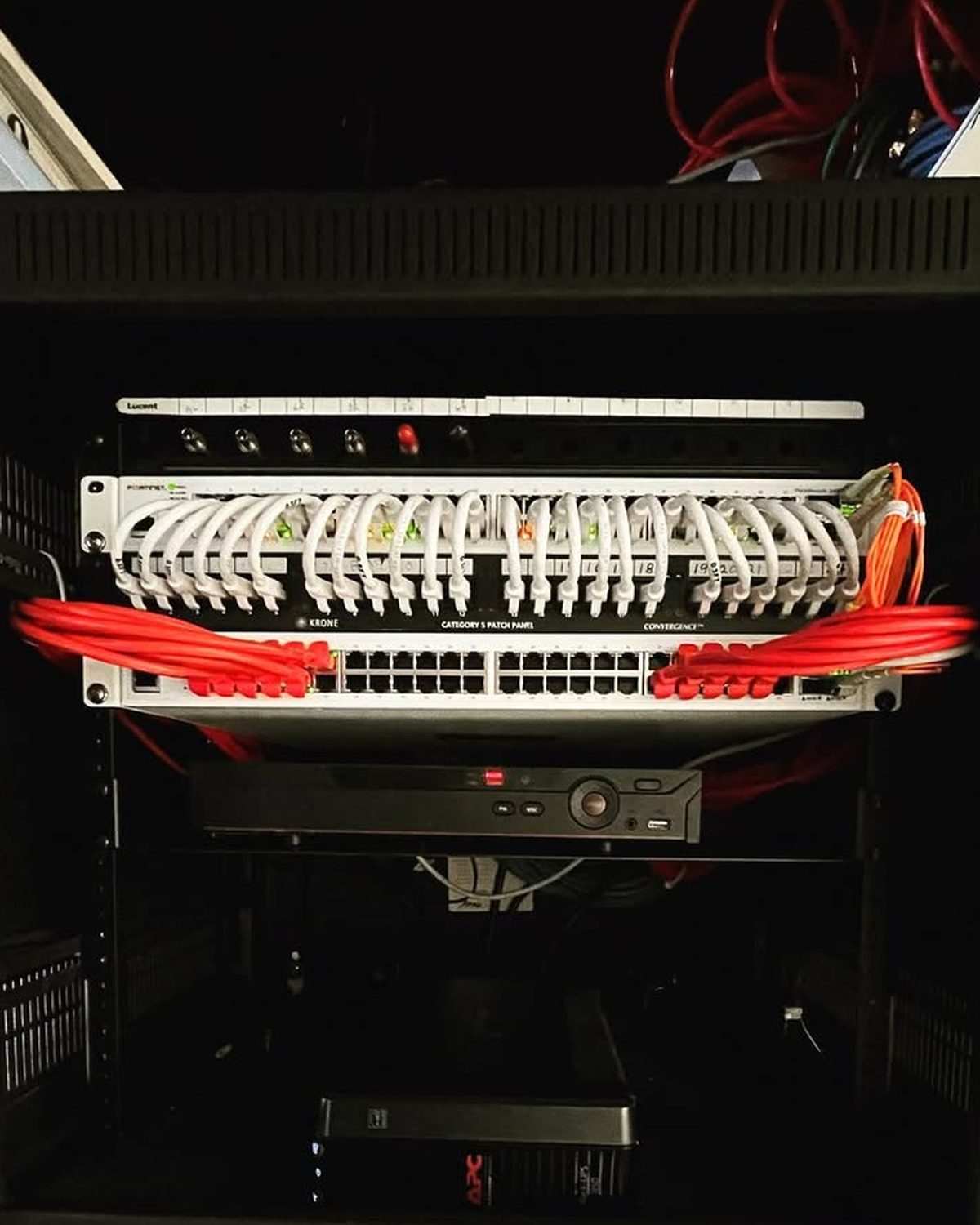 The same network cabinet after cleanup, with white patch cords dressed in an even arc off the patch panel