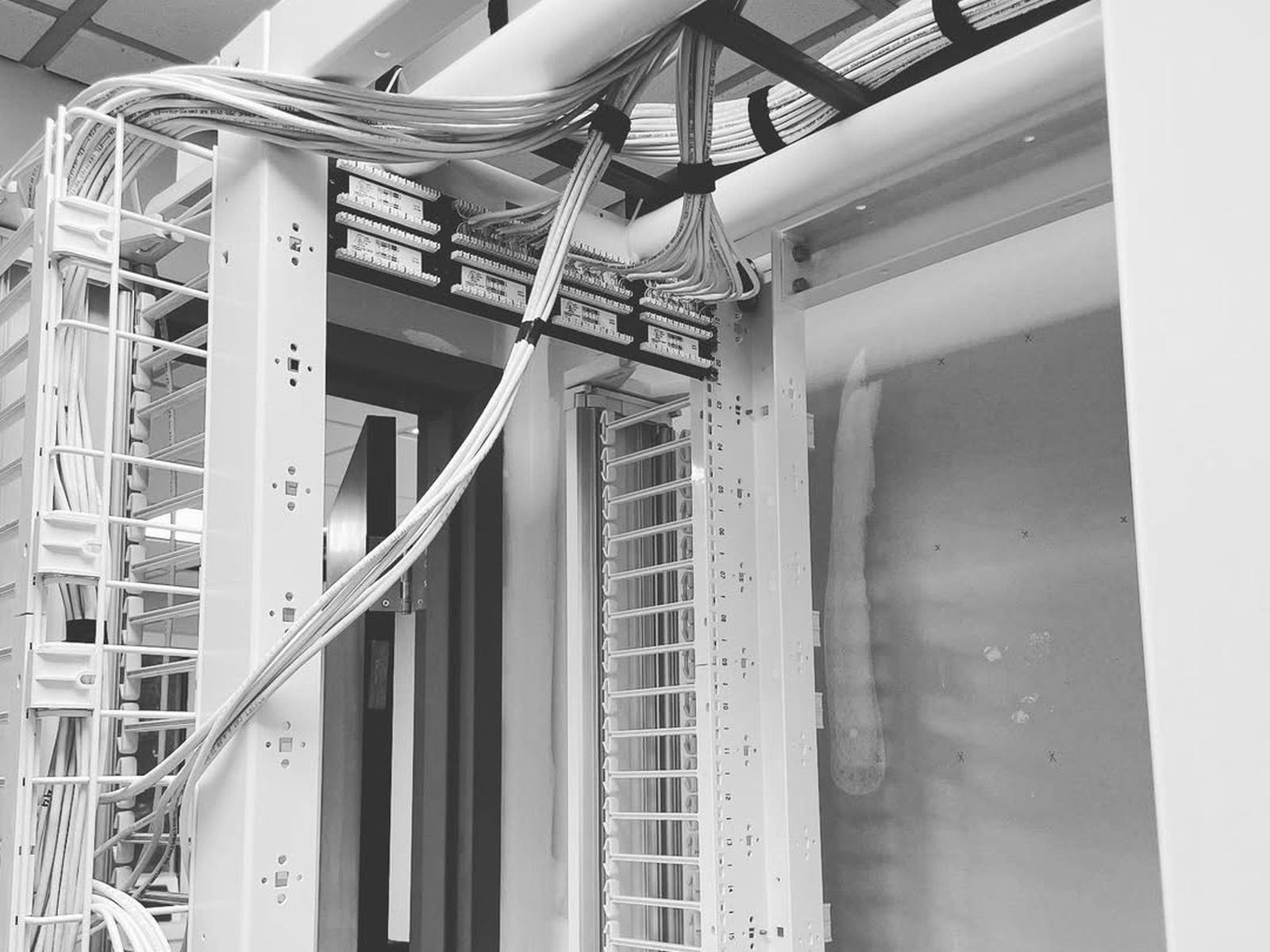 Open network rack with white patch cords dressed through vertical cable managers below an overhead cable tray